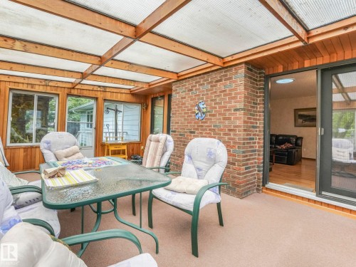 Enclosed sunroom featuring a transparent panel roof, wood-paneled walls, brick accents, and a sliding glass door - 11921 231 Street, Edmonton, AB 