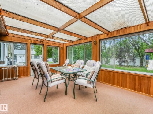 Sunroom featuring wood paneling, extensive window walls, translucent ceiling panels, and neutral carpeting - 11921 231 Street, Edmonton, AB 