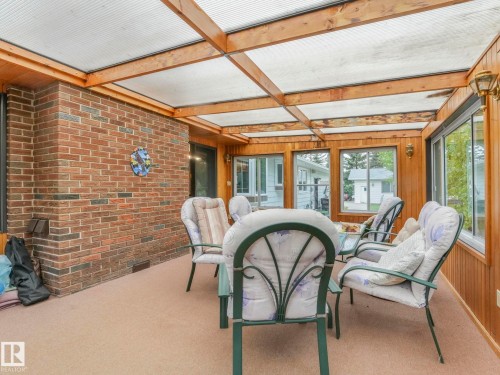 Enclosed sunroom featuring a brick accent wall, wood-paneled walls, and a translucent panel roof with exposed wood beams - 11921 231 Street, Edmonton, AB 