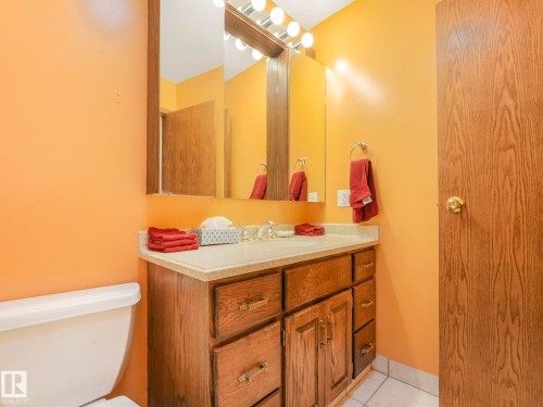 Bathroom featuring a vanity with wood-finish cabinetry, a light-colored countertop with an integrated sink, and a rectangular mirror - 11921 231 Street, Edmonton, AB 