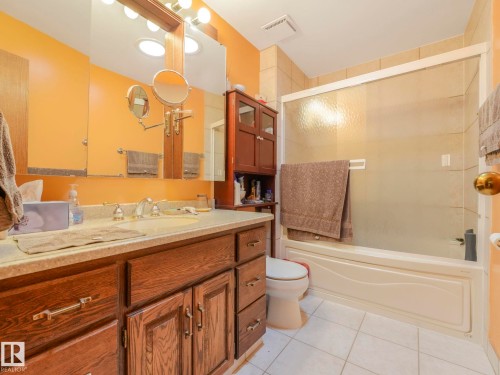 Bathroom featuring a full vanity with wood-finish cabinetry, a large mirror, a combined shower and tub with a sliding glass enclosure, and white tile flooring - 11921 231 Street, Edmonton, AB 