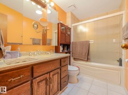 Bathroom featuring a full vanity with wood-finish cabinetry, a large mirror, a combined shower and tub with a sliding glass enclosure, and white tile flooring - 