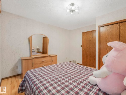 Bedroom featuring wood-finish flooring, textured wallpaper, a ceiling-mounted light fixture, and two wood-paneled doors - 11921 231 Street, Edmonton, AB 