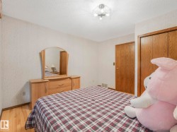 Bedroom featuring wood-finish flooring, textured wallpaper, a ceiling-mounted light fixture, and two wood-paneled doors - 