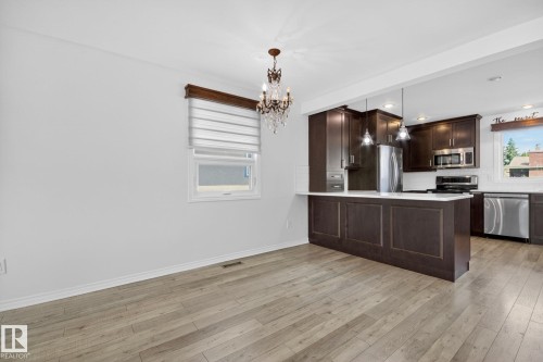 Open-concept kitchen and dining area featuring light wood-finish flooring, a decorative chandelier, dark wood cabinetry, stainless steel appliances, and a kitchen island with pendant lighting - 3 Galaxy Way, Sherwood Park, AB 