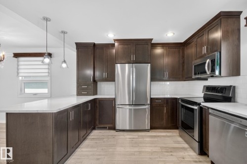 Modern kitchen featuring dark wood-finish cabinetry, stainless steel appliances, light countertops, a white subway tile backsplash, and light wood-finish flooring - 3 Galaxy Way, Sherwood Park, AB 