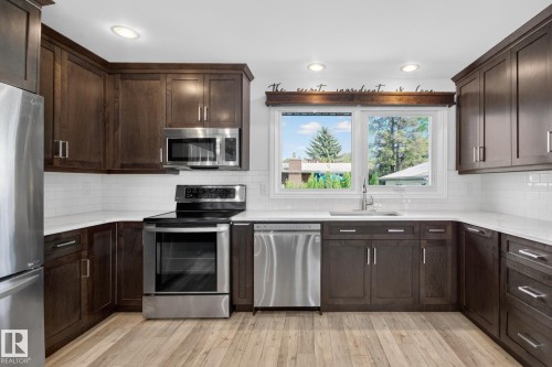Modern kitchen featuring dark wood cabinetry, stainless steel appliances, white subway tile backsplash, and light wood-finish flooring - 3 Galaxy Way, Sherwood Park, AB 