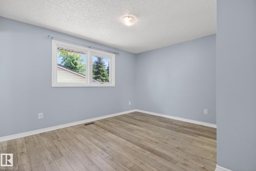 Bright room featuring a window with white trim, light blue wall paint, wood-finish flooring, white baseboards, and a ceiling-mounted light fixture - 3 Galaxy Way, Sherwood Park, AB 