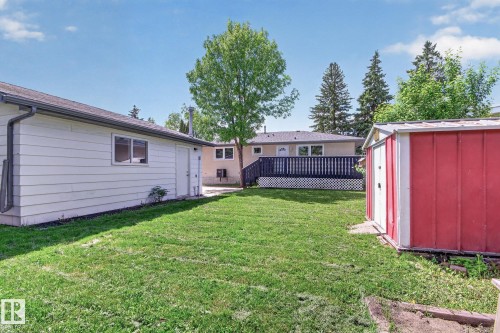 Expansive backyard featuring a green lawn, a red storage shed, a multi-level deck with lattice skirting, and mature trees - 3 Galaxy Way, Sherwood Park, AB 