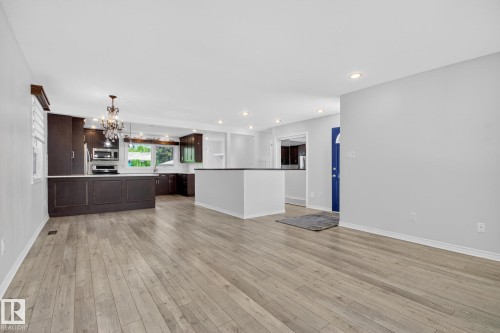 Open-concept living space featuring wood-finish flooring, recessed lighting, and a kitchen with dark cabinetry and a crystal chandelier - 3 Galaxy Way, Sherwood Park, AB 