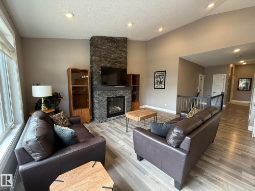 Living area featuring a floor-to-ceiling stone fireplace, vaulted ceiling, recessed lighting, wood-finish flooring, and a window with white trim - 2 104 Allard Link, Edmonton, AB 