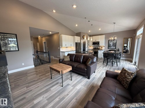 Open-concept living space featuring wood-finish flooring, a vaulted ceiling, recessed lighting, and a contemporary kitchen with white cabinetry and dark countertops - 2 104 Allard Link, Edmonton, AB 