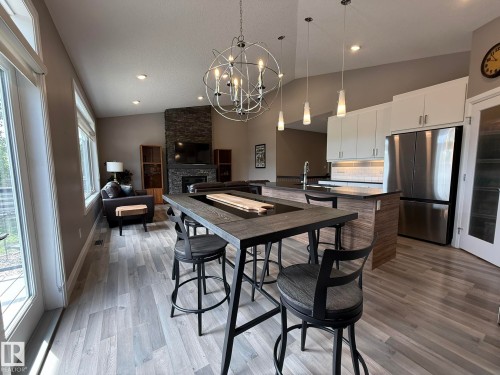 Open-concept living area featuring wood-finish flooring, a stone-clad fireplace, and a contemporary kitchen - 2 104 Allard Link, Edmonton, AB 