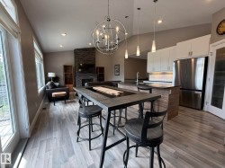 Open-concept living area featuring wood-finish flooring, a stone-clad fireplace, and a contemporary kitchen - 