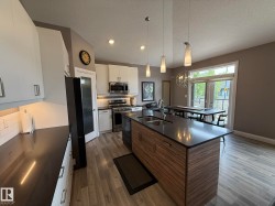 Modern kitchen featuring an island with wood-finish cabinetry and a dark countertop, stainless steel appliances, white subway tile backsplash, and light wood-finish flooring - 