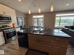 Open-concept kitchen featuring an island with a double basin sink, dark countertop, and wood-finish cabinetry - 