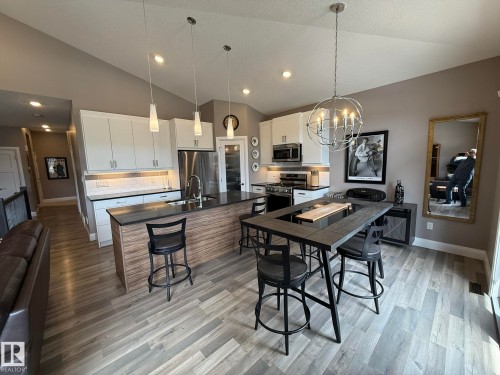 Open-concept kitchen featuring wood-finish flooring, vaulted ceilings, white cabinetry, dark countertops, and stainless steel appliances - 2 104 Allard Link, Edmonton, AB 