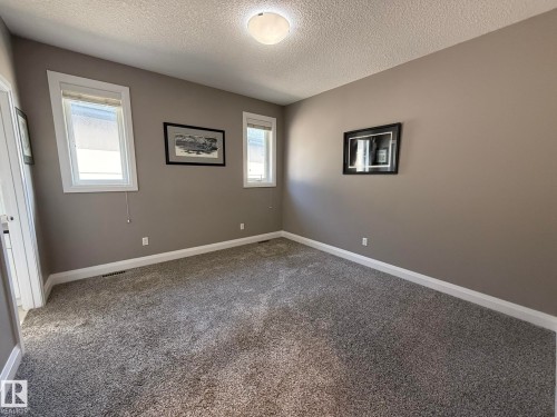 Neutral-toned room featuring two windows with white trim, a textured ceiling, and gray carpeting - 2 104 Allard Link, Edmonton, AB 