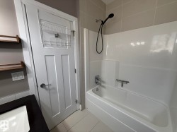 Bathroom featuring a white bathtub and shower combination with a black shower head, light grey wall tiles, and white floor tiles - 
