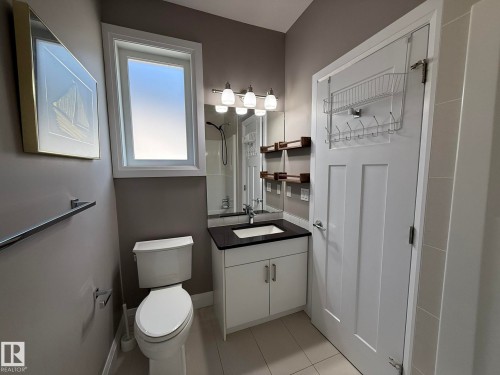 Bathroom featuring a white vanity with a dark countertop and undermount sink, a white toilet, and a window with white trim - 2 104 Allard Link, Edmonton, AB 