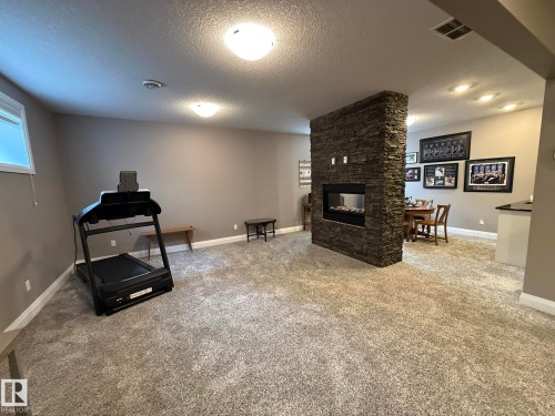 Open-concept finished lower level featuring a stone-clad fireplace with a linear insert, plush carpet flooring, recessed lighting, and a built-in bar area with a dark countertop - 2 104 Allard Link, Edmonton, AB 