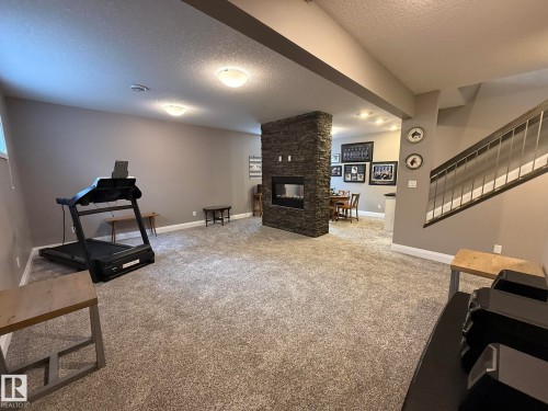 Spacious lower-level area featuring textured carpeting, a stone-clad fireplace with an integrated linear firebox, and a contemporary staircase with metal railings - 2 104 Allard Link, Edmonton, AB 