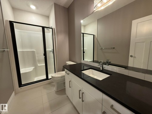 Basement Contemporary bathroom featuring a black-framed glass shower enclosure, a vanity with a dark countertop and integrated sink, a large wall-mounted mirror, and white flat-panel cabinetry with brushed nickel hardware - 2 104 Allard Link, Edmonton, AB 
