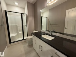 Basement Contemporary bathroom featuring a black-framed glass shower enclosure, a vanity with a dark countertop and integrated sink, a large wall-mounted mirror, and white flat-panel cabinetry with brushed nickel hardware - 