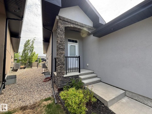 Front entry featuring a stone-clad column, concrete steps, and a black metal railing - 2 104 Allard Link, Edmonton, AB 