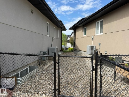 Fenced side yard featuring a gravel surface, window wells, and exterior stucco finishes - 2 104 Allard Link, Edmonton, AB 