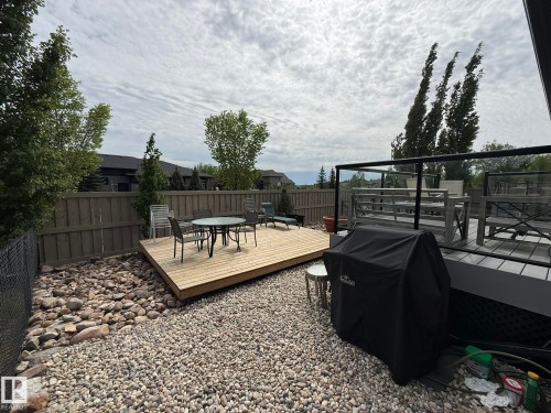 Multi-level outdoor living space featuring a ground-level wood deck and an elevated composite deck with glass panel railings - 2 104 Allard Link, Edmonton, AB 