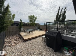 Multi-level outdoor living space featuring a ground-level wood deck and an elevated composite deck with glass panel railings - 