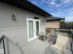 Upper-level balcony featuring composite decking, white French doors, and black metal railings - 