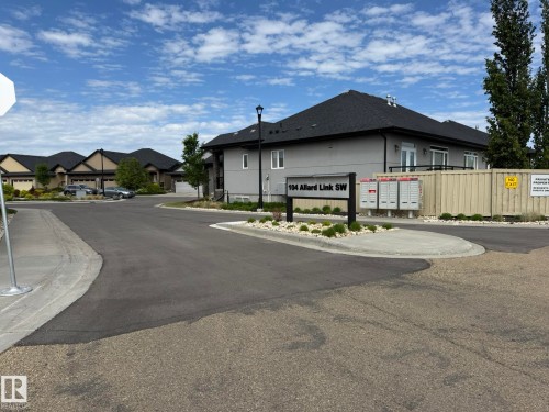Modern residential community entrance featuring a street sign with property address, multiple mailboxes, and a neutral-toned building with dark roofing - 2 104 Allard Link, Edmonton, AB 