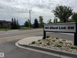 Street signage for 104 Allard Link SW featuring a landscaped base with river rock and low-lying shrubs - 
