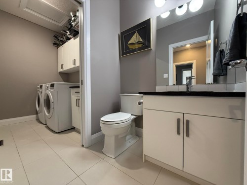 Integrated laundry area featuring white tile flooring, built-in cabinetry, and a vanity with a dark countertop - 2 104 Allard Link, Edmonton, AB 