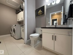 Integrated laundry area featuring white tile flooring, built-in cabinetry, and a vanity with a dark countertop - 