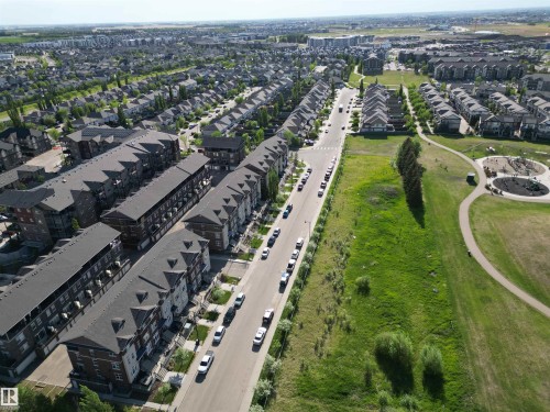 Aerial view showcasing a residential community with rows of multi-story townhomes featuring dark roofs and light-colored facades - 2 104 Allard Link, Edmonton, AB 