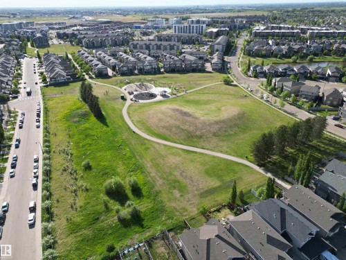 Expansive green space featuring a paved walking path, open fields, and a designated playground area - 2 104 Allard Link, Edmonton, AB 