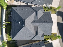 Multi-pitched roofline featuring dark gray shingles, multiple vents, and a perimeter of manicured landscaping - 