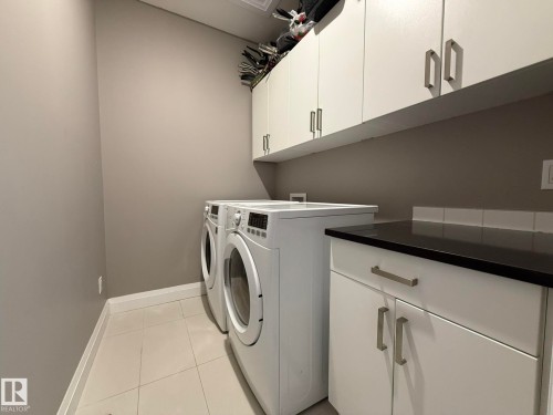 Dedicated utility area featuring white cabinetry with brushed nickel hardware, a black countertop, and a white subway tile backsplash - 2 104 Allard Link, Edmonton, AB 