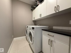 Dedicated utility area featuring white cabinetry with brushed nickel hardware, a black countertop, and a white subway tile backsplash - 