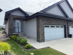 Modern exterior featuring a stone facade, a single garage door with upper window panels, a front entry with a black railing, a concrete walkway, and landscaped garden beds - 
