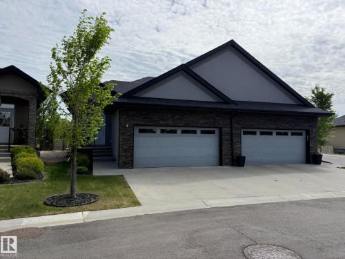 Contemporary exterior featuring dark stacked stone accents, a dark asphalt shingle roof, and a light gray gable - 2 104 Allard Link, Edmonton, AB 