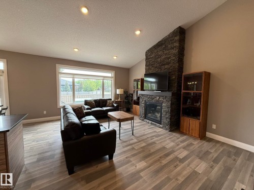 Spacious living area featuring vaulted ceilings, recessed lighting, a large picture window, and wood-finish flooring - 2 104 Allard Link, Edmonton, AB 