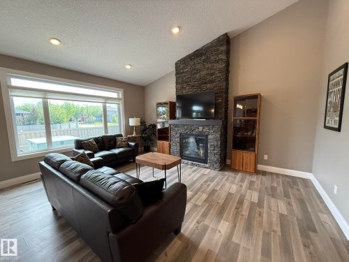 Spacious living area featuring a stone-clad fireplace with a recessed hearth, a dark wood mantle, and a mounted television - 2 104 Allard Link, Edmonton, AB 