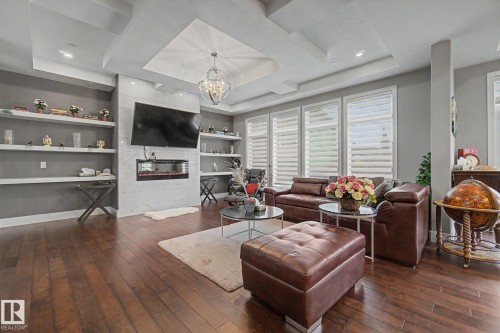 Spacious living area featuring wood-finish flooring, a tray ceiling with recessed lighting and a chandelier, and a fireplace with a tiled surround - 3036 59 Avenue, Rural Leduc County, AB 