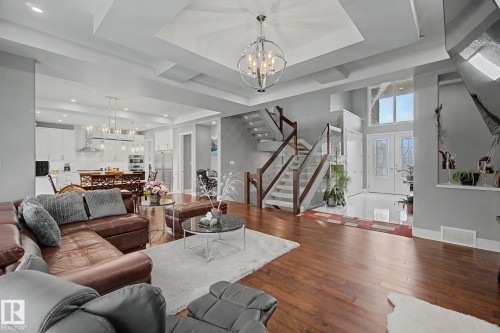Open-concept living space featuring wood-finish flooring, a contemporary staircase with glass railing, a double-height entryway with transom windows, and a large kitchen with white cabinetry and stainless steel appliances - 3036 59 Avenue, Rural Leduc County, AB 