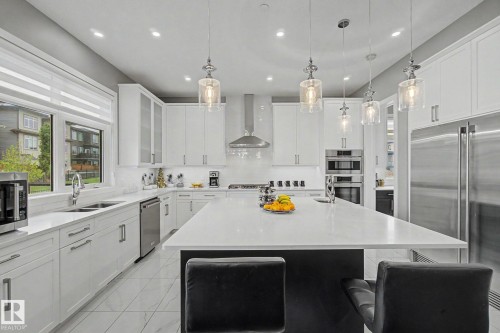 Gourmet kitchen with a large central island, white cabinetry, integrated stainless steel appliances, pendant lighting, and tiled flooring - 3036 59 Avenue, Rural Leduc County, AB 