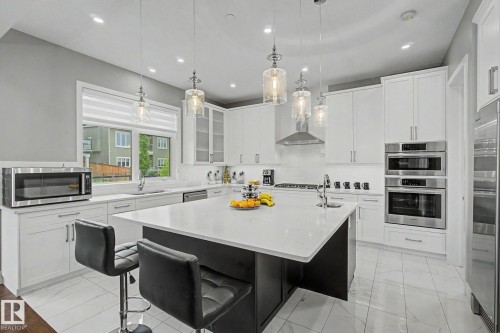 Modern kitchen featuring a large central island with a solid surface countertop, white shaker-style cabinetry, stainless steel appliances, and pendant lighting - 3036 59 Avenue, Rural Leduc County, AB 